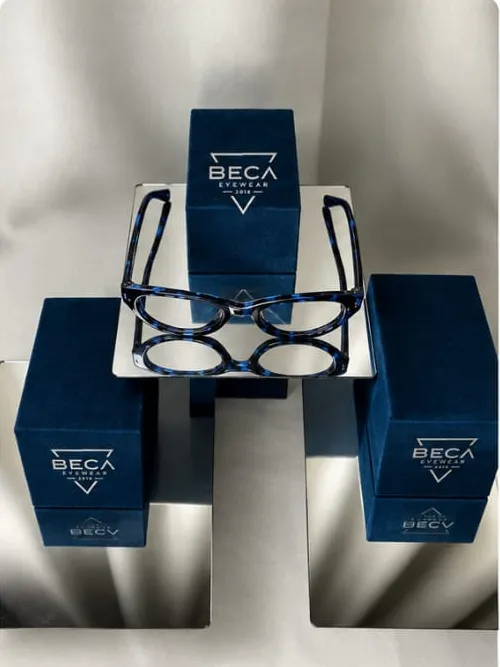 Óculos de acetato sobre as caixas azuis da BECA, em expositores espelhados.